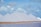 Large, symmetrical white pyramids of salt stand in a line against a backdrop of a partly cloudy sky. The foreground features a body of water with a calm surface and a strip of sandy ground.