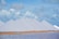 Large, symmetrical white pyramids of salt stand in a line against a backdrop of a partly cloudy sky. The foreground features a body of water with a calm surface and a strip of sandy ground.