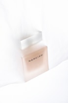 A perfume bottle labeled 'NARCISO' is positioned against a soft, light background. The bottle has a minimalistic design with clean lines and a slightly frosted appearance.