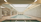 A luxurious indoor swimming pool with a serene and elegant design. The pool is surrounded by marble tiles and has a high ceiling with skylights allowing natural light to illuminate the space. Loungers and tables are positioned around the pool in a spacious, symmetrical arrangement. Ornate architectural details and muted colors create a sophisticated atmosphere.