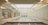 A luxurious indoor swimming pool with a serene and elegant design. The pool is surrounded by marble tiles and has a high ceiling with skylights allowing natural light to illuminate the space. Loungers and tables are positioned around the pool in a spacious, symmetrical arrangement. Ornate architectural details and muted colors create a sophisticated atmosphere.
