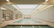 A luxurious indoor swimming pool with a serene and elegant design. The pool is surrounded by marble tiles and has a high ceiling with skylights allowing natural light to illuminate the space. Loungers and tables are positioned around the pool in a spacious, symmetrical arrangement. Ornate architectural details and muted colors create a sophisticated atmosphere.