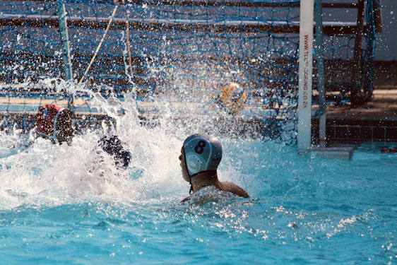 A dynamic action shot of young female water polo players celebrating a goal in a sunlit pool.