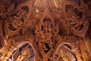 Intricately carved wooden interior featuring detailed figures and ornate patterns, reminiscent of traditional Eastern art and architecture. The craftsmanship showcases complex motifs and human-like figures interwoven with decorative elements.