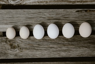 Six eggs are arranged in a line on a rustic wooden surface, showing a gradient of sizes.