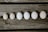 Six eggs are arranged in a line on a rustic wooden surface, showing a gradient of sizes.