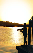 A fisherman casting a line into a serene lake during golden hour.