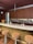 A modern bar setup features a sleek marble countertop with brown textured stools. Behind the bar, a wall showcases a variety of liquor bottles. Decorative items include two intricately designed skulls and a vase with vibrant orange flowers. The wooden cabinetry adds warmth to the space.