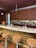 A modern bar setup features a sleek marble countertop with brown textured stools. Behind the bar, a wall showcases a variety of liquor bottles. Decorative items include two intricately designed skulls and a vase with vibrant orange flowers. The wooden cabinetry adds warmth to the space.