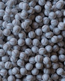 A large pile of baseballs fills the entire frame, with each ball showing visible red stitching. The baseballs are arranged closely together, creating a textured pattern.
