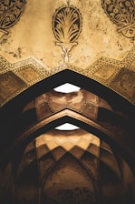 Ornate arches adorned with intricate geometric patterns and floral designs in a muted, earthy tone. The architecture features detailed craftsmanship with a distinct historical and cultural influence.