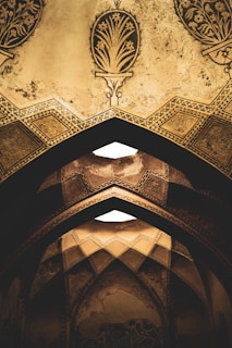 Ornate arches adorned with intricate geometric patterns and floral designs in a muted, earthy tone. The architecture features detailed craftsmanship with a distinct historical and cultural influence.