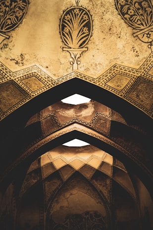 Ornate arches adorned with intricate geometric patterns and floral designs in a muted, earthy tone. The architecture features detailed craftsmanship with a distinct historical and cultural influence.
