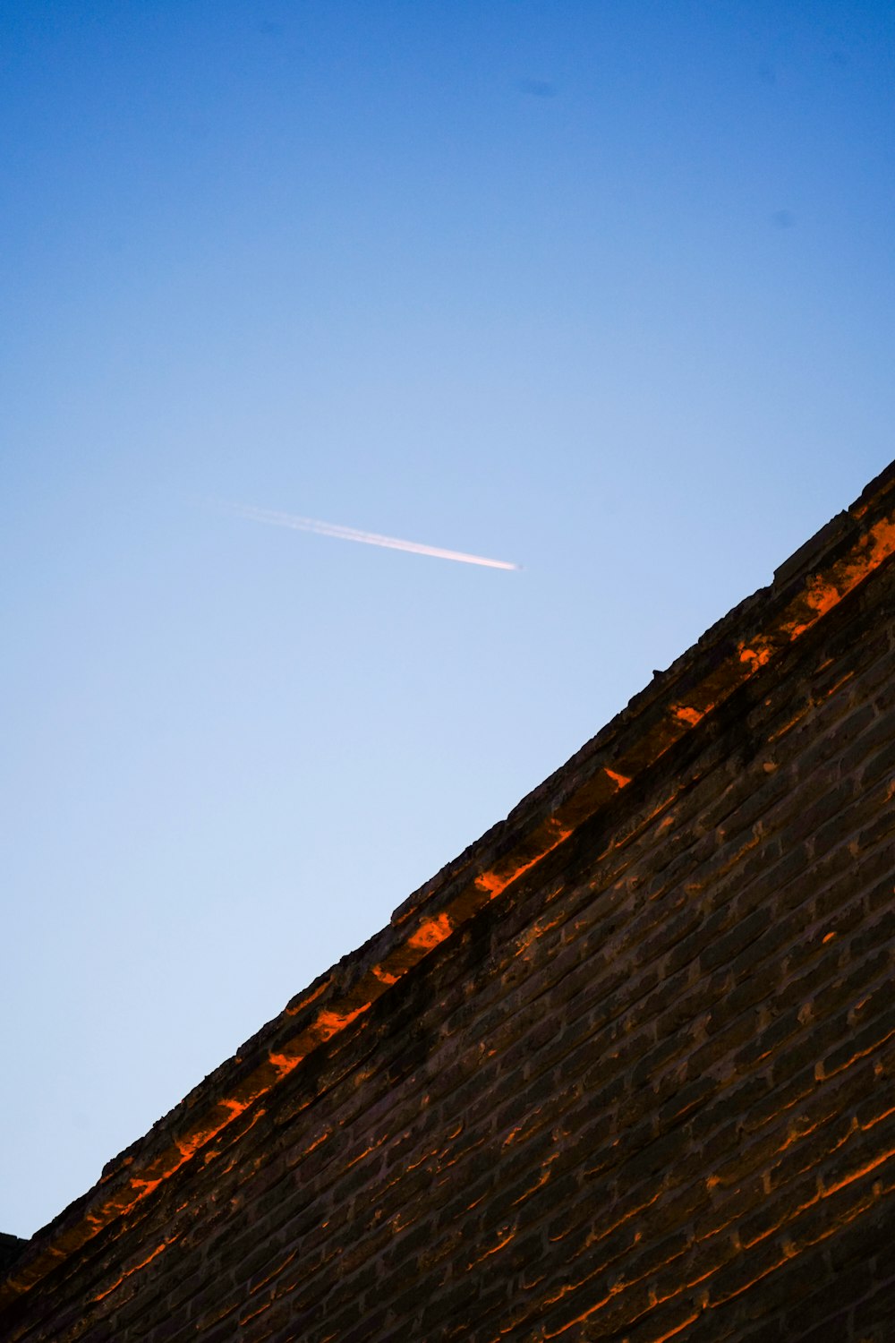 a jet flying over a brick wall under a blue sky