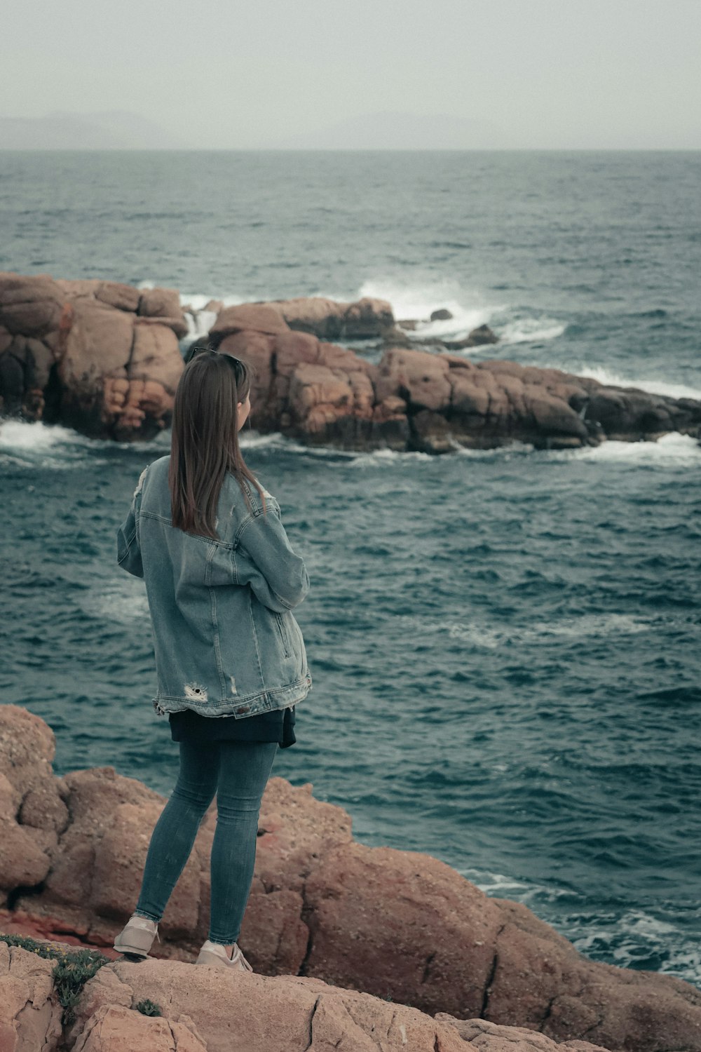 a woman standing on a rocky shore next to the ocean
