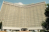 A large hotel building with a concave facade covered in numerous identical rectangular windows. The structure is prominently labeled 'Hotel Uzbekistan' at the top and has a symmetrical, grid-like pattern.