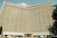 A large hotel building with a concave facade covered in numerous identical rectangular windows. The structure is prominently labeled 'Hotel Uzbekistan' at the top and has a symmetrical, grid-like pattern.