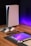 A sleek, modern setup featuring a gaming console with two controllers on a wooden surface. Nearby are a smartphone, smartwatch, tablet with a vivid screen, wireless earbuds, and a stylus. The background is illuminated with a soft purple glow.