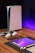 A sleek, modern setup featuring a gaming console with two controllers on a wooden surface. Nearby are a smartphone, smartwatch, tablet with a vivid screen, wireless earbuds, and a stylus. The background is illuminated with a soft purple glow.