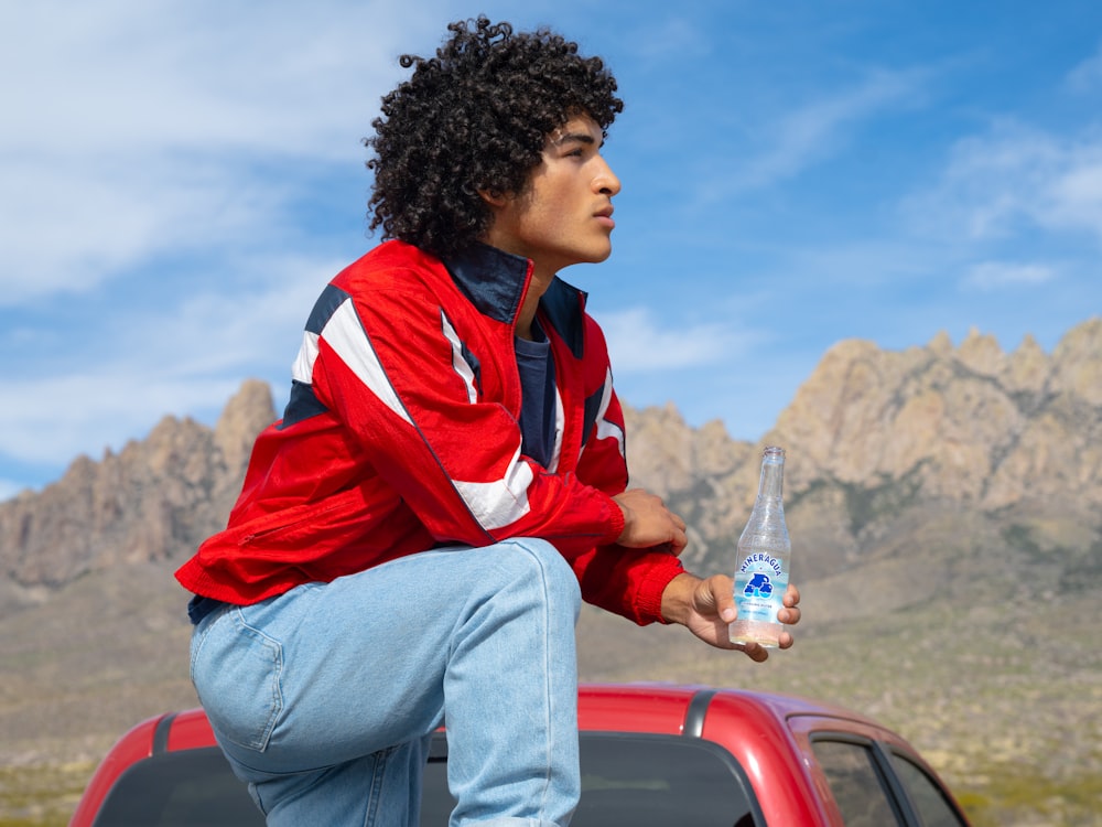 a man with a bottle of water sitting on the hood of a red truck