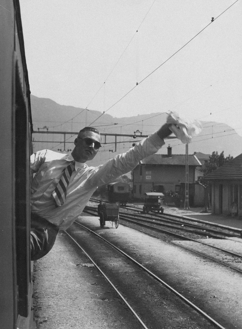 a black and white photo of a man leaning out of a train window