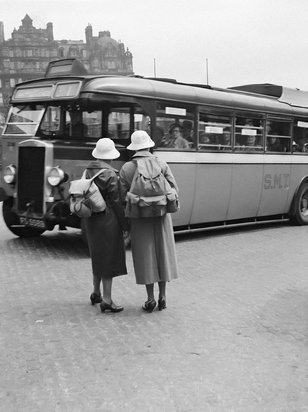 a black and white photo of two women standing in front of a bus