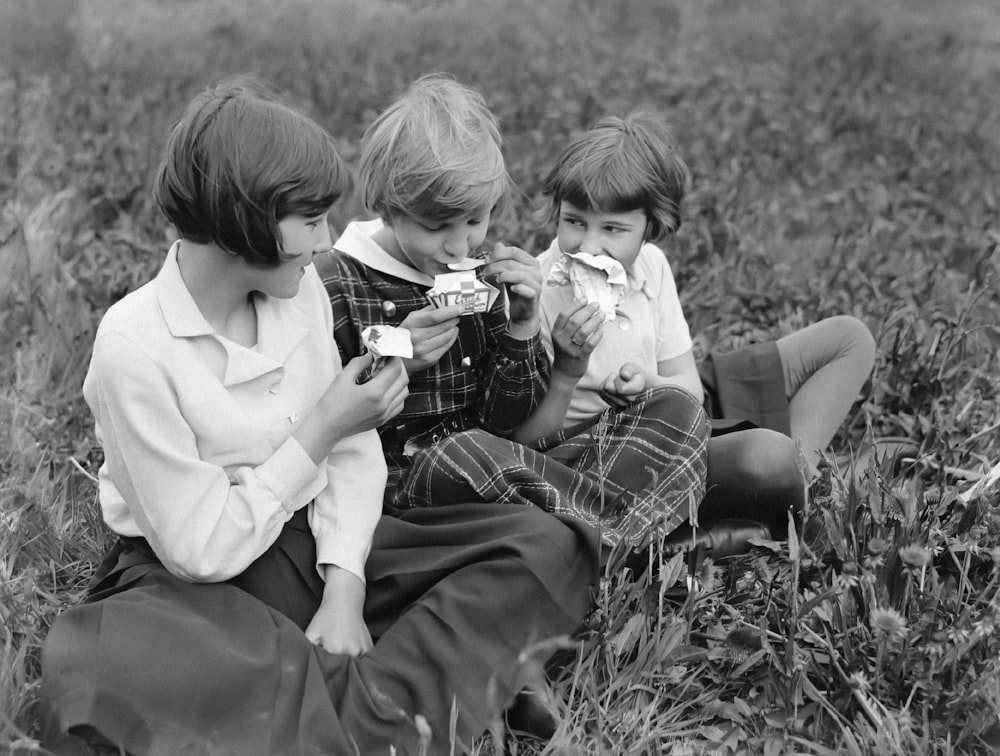 three young children sitting in a field eating food