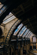 An intricately designed interior featuring arched ceilings and skylights in a historic building. The architecture showcases detailed brickwork, ornamental patterns, and large windows that allow natural light to illuminate the space.