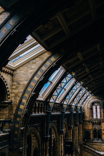 An intricately designed interior featuring arched ceilings and skylights in a historic building. The architecture showcases detailed brickwork, ornamental patterns, and large windows that allow natural light to illuminate the space.