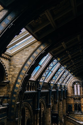 An intricately designed interior featuring arched ceilings and skylights in a historic building. The architecture showcases detailed brickwork, ornamental patterns, and large windows that allow natural light to illuminate the space.