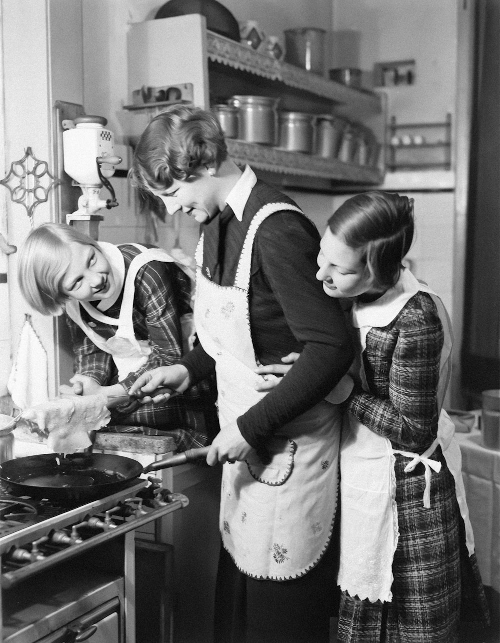 uma foto em preto e branco de três mulheres cozinhando em uma cozinha