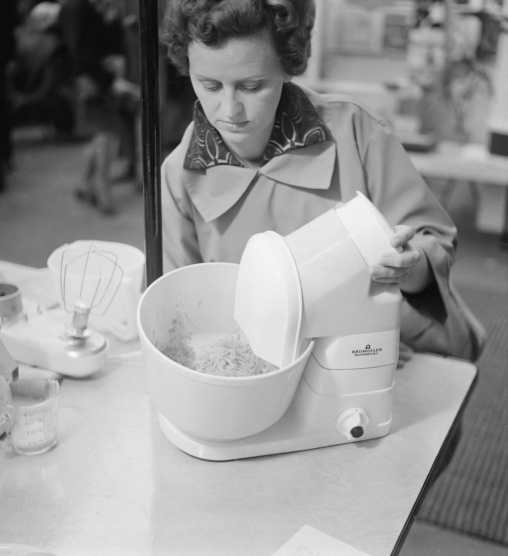 a black and white photo of a woman pouring something into a bowl