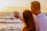 Smiling middle-aged couple standing in front of their new beachfront property at sunset.