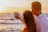 Smiling middle-aged couple standing in front of their new beachfront property at sunset.