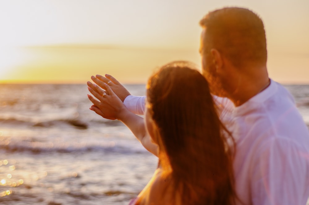 um homem e uma mulher em pé em uma praia ao pôr do sol