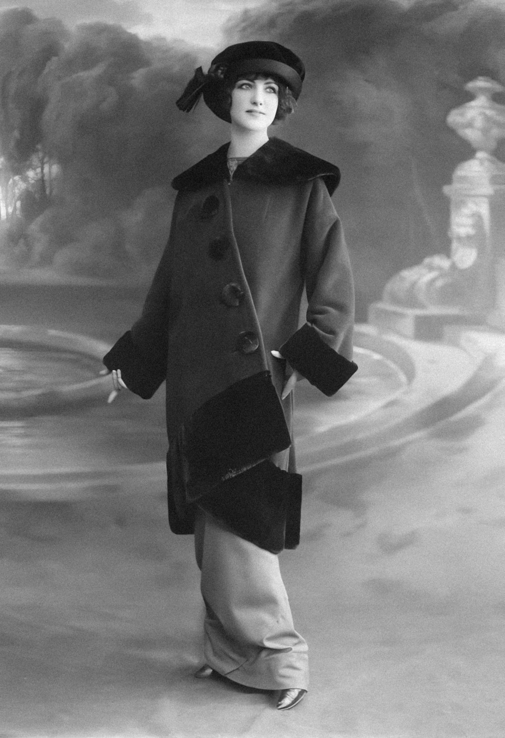 a black and white photo of a woman in a coat and hat