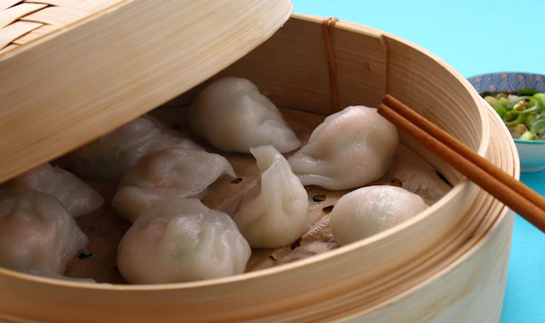 Freshly steamed momos being lifted with chopsticks, steam swirling in the air.