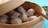 A bamboo steamer containing several steamed dumplings, partially open to reveal the contents. A pair of chopsticks rests on the edge of the steamer. In the background, there is a small bowl with sliced spring onions.