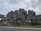 An architectural structure composed of stacked modular concrete units, creating a geometric and futuristic appearance. The building features numerous windows and terraces, surrounded by some sparse landscaping and trees.