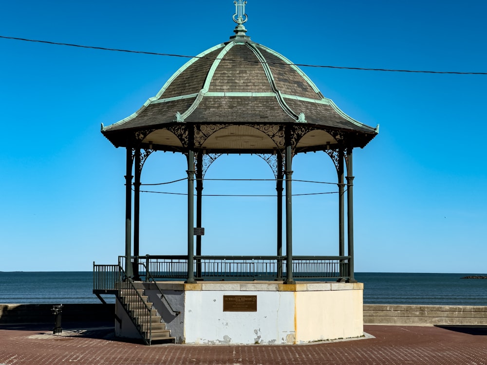 a gazebo sitting on top of a brick walkway next to the ocean