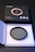 A circular camera filter placed inside an open, white, protective case made of foam. The filter is labeled with specifications and brand details. Accompanying the filter is a black and orange product box with graphical elements and text indicating high-definition optical glass.