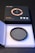A circular camera filter placed inside an open, white, protective case made of foam. The filter is labeled with specifications and brand details. Accompanying the filter is a black and orange product box with graphical elements and text indicating high-definition optical glass.