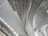 Curved and linear metal structures form an intricate roof design. The architecture appears modern with a focus on geometric patterns and clean lines. The ceiling panels reflect light, adding a sense of brightness and spaciousness to the area.