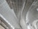 Curved and linear metal structures form an intricate roof design. The architecture appears modern with a focus on geometric patterns and clean lines. The ceiling panels reflect light, adding a sense of brightness and spaciousness to the area.