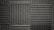 A pattern of black acoustic foam panels arranged in a grid. Each panel features alternating horizontal and vertical grooves, creating a textured appearance that absorbs sound. The lighting emphasizes the texture and depth of the grooves.