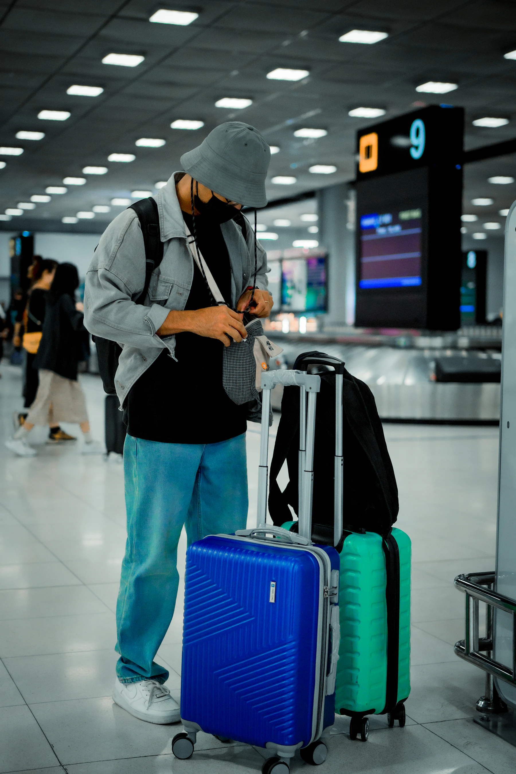 Traveler standing in an airport with rolling luggage and a travel bag