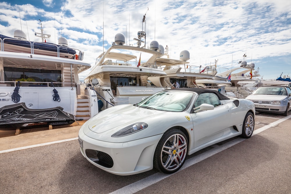 a white sports car parked in front of a yacht