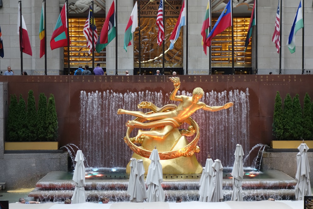 a golden statue in front of a fountain with flags in the background