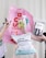 Several hands are holding various gardening and plant care products against a light background. These include a pink banner with bold red text, a bottle of plant spray, gardening tags, bottles of liquid fertilizer, and bags of plant soil labeled in German.