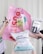 Several hands are holding various gardening and plant care products against a light background. These include a pink banner with bold red text, a bottle of plant spray, gardening tags, bottles of liquid fertilizer, and bags of plant soil labeled in German.